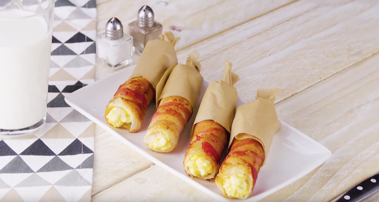 Vier Toast-Ei-Bacon-Rollen auf weiÃŸem Teller in Backpapier gewickelt