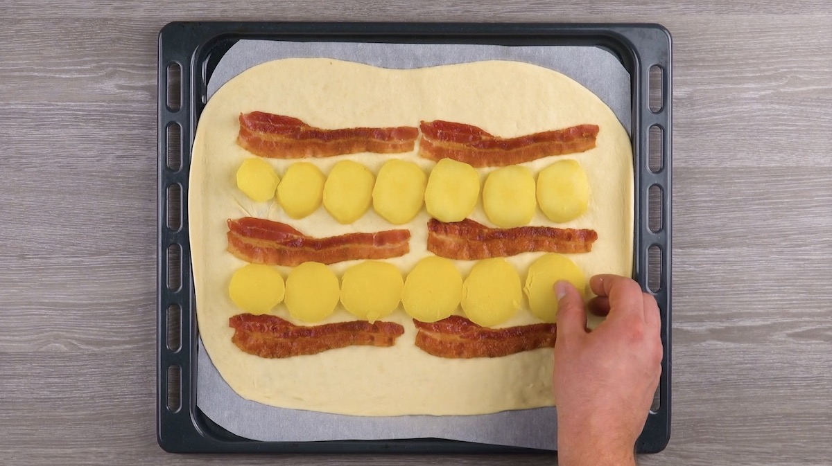 Zwischen Baconscheiben auf Pizzateig werden Kartoffelscheiben gelegt