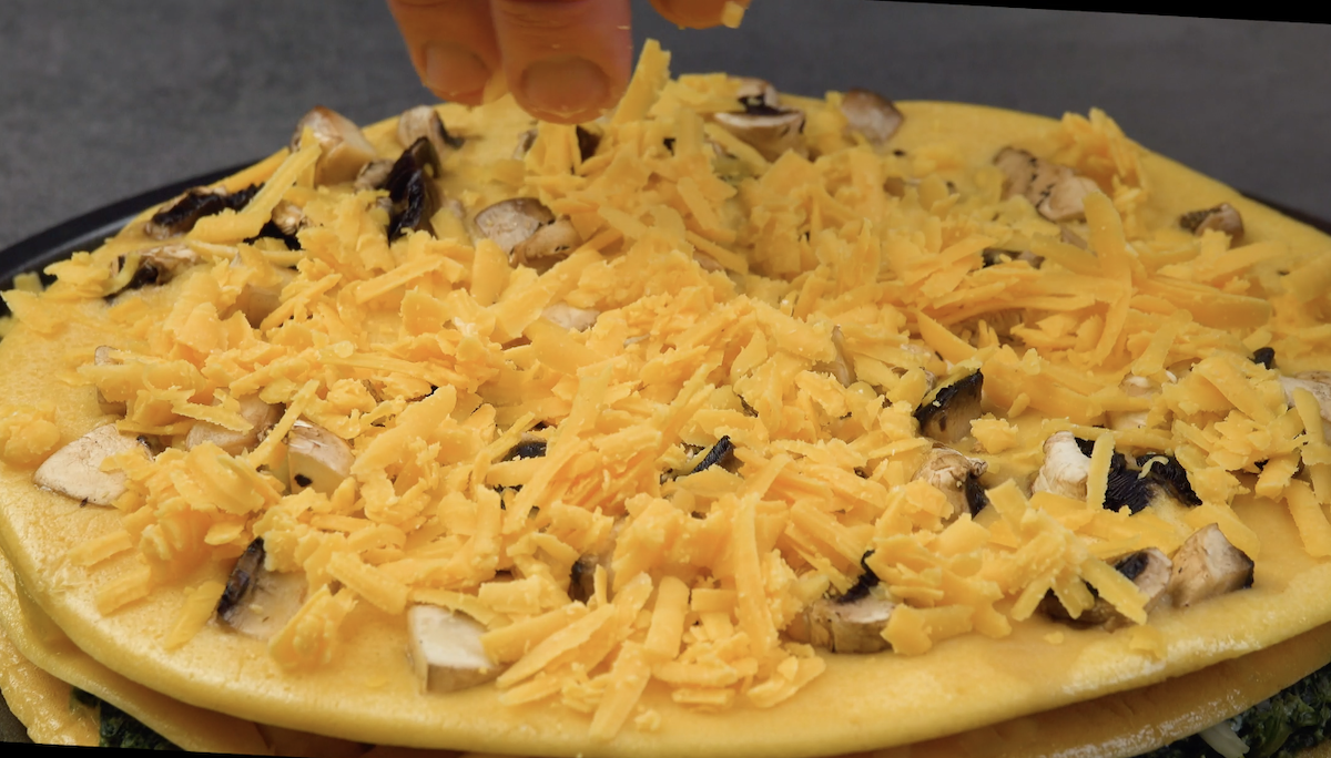 Champignons und geriebener Cheddar werden auf weiterem Omelett-Pfannkuchen verteilt
