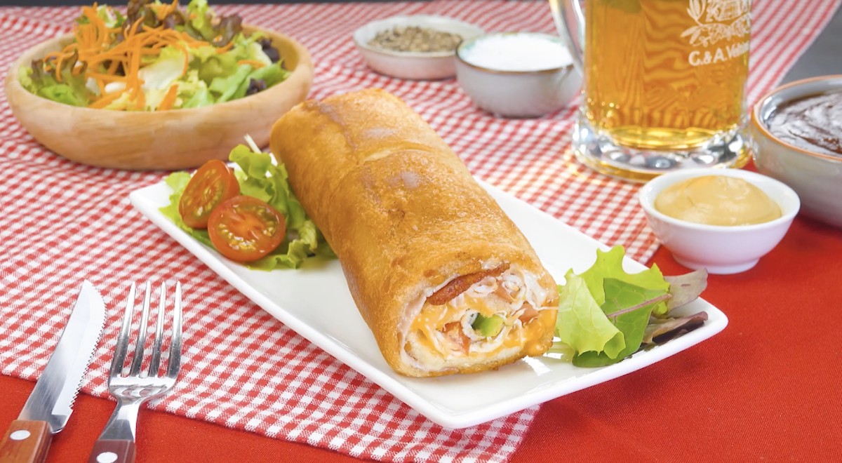 Club-Sandwich-Rolle mit Bacon, Avocado und Cheddar auf Teller, daneben Salat und ein Bier