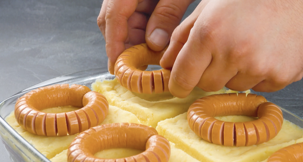 Eine Wurst-Spirale wird auf Kartoffelstampf in eine Auflaufform gelegt