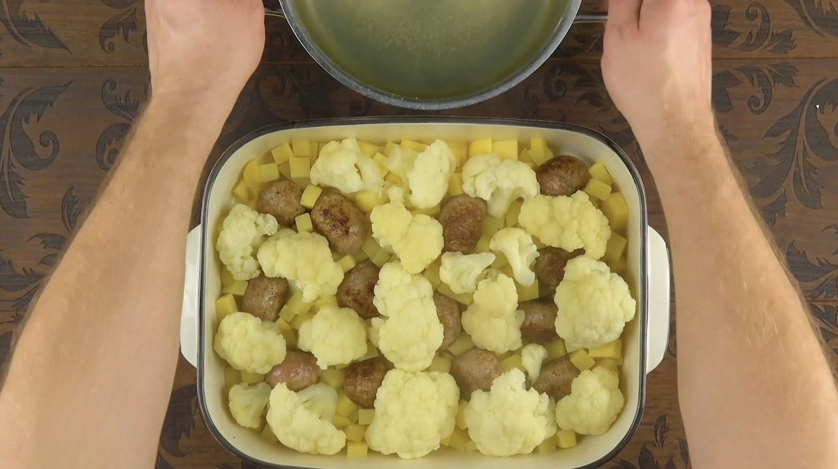 Blumenkohlröschen werden auf Kartoffeln und Bratwurstbällchen in Auflaufform verteilt