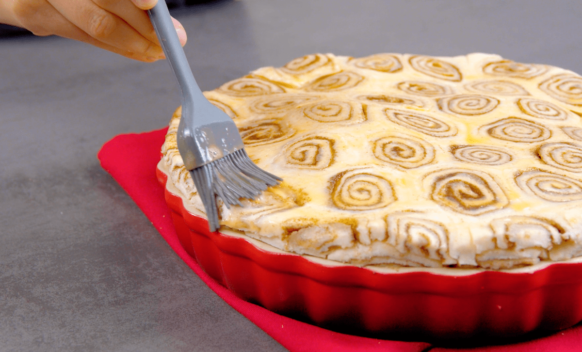 Eine Teigschicht aus Zimtschnecken wird mit verquirltem Ei bestrichen