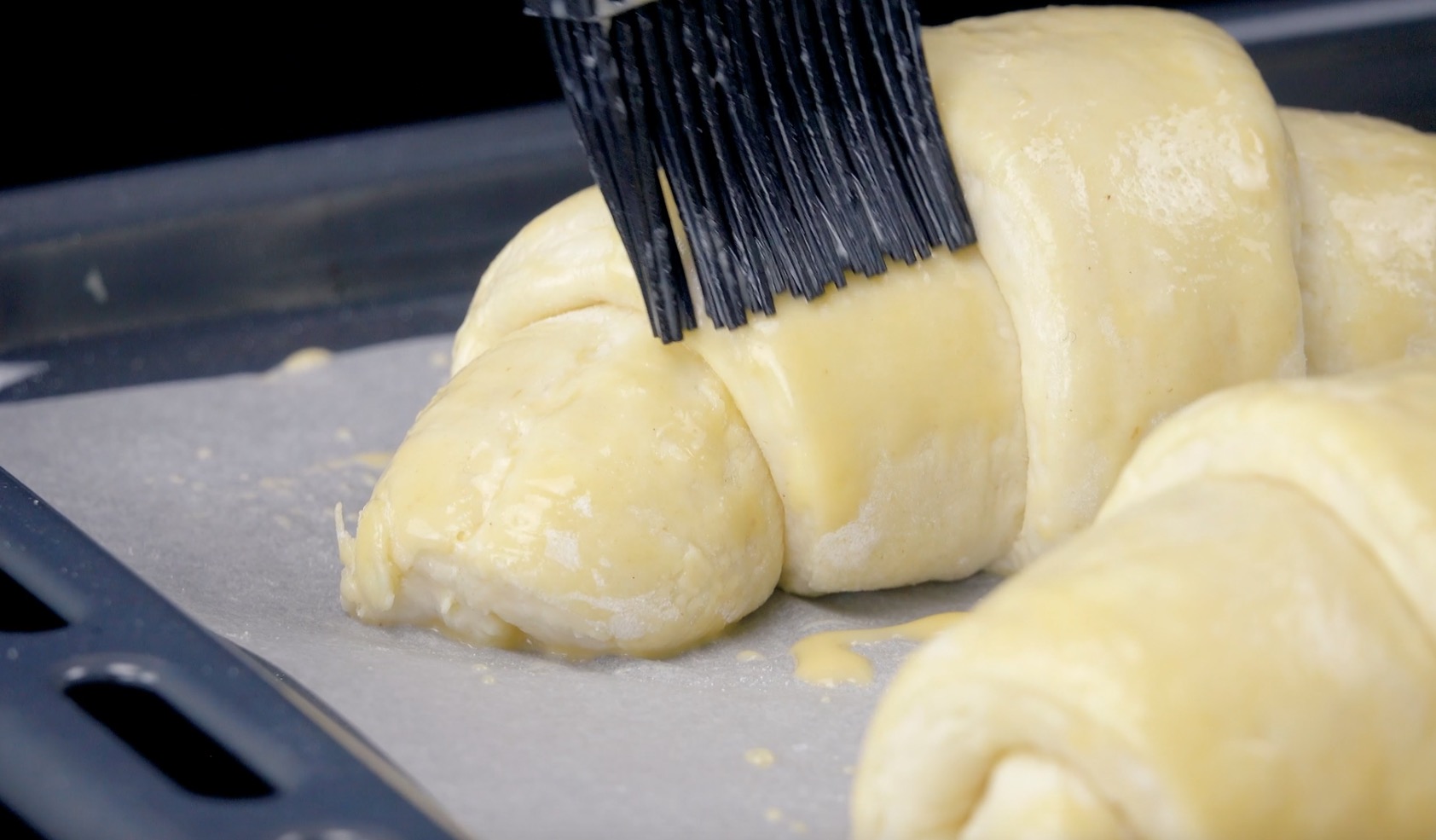 Aufgerollte Croissants werden mit verquirltem Ei und Milch bepinselt