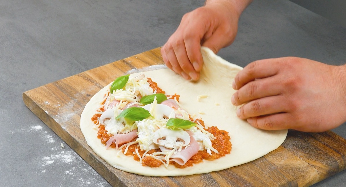 Pizzateig wird zur HÃ¤lfte mit Salsiccia und Burrata belegt und zusammengeklappt
