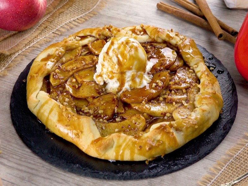 Apfel-Karamell-Dessert auf einem Teller. Ein Nudelholz liegt als Dekoration daneben.