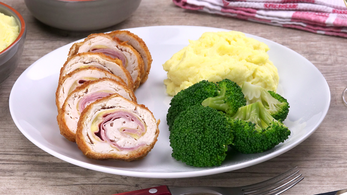 In Scheiben geschnittenes Hühnchen-Cordon-Bleu mit Béchamelcreme, Kartoffelbreu und Brokkoli auf einem Teller.