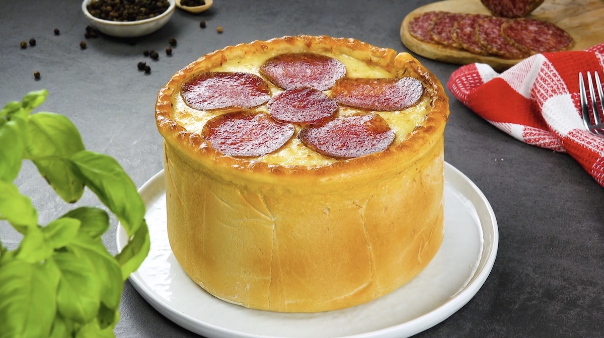 Ein Pizzakuchen auf einem Teller, mit Zutaten im Hintergrund.
