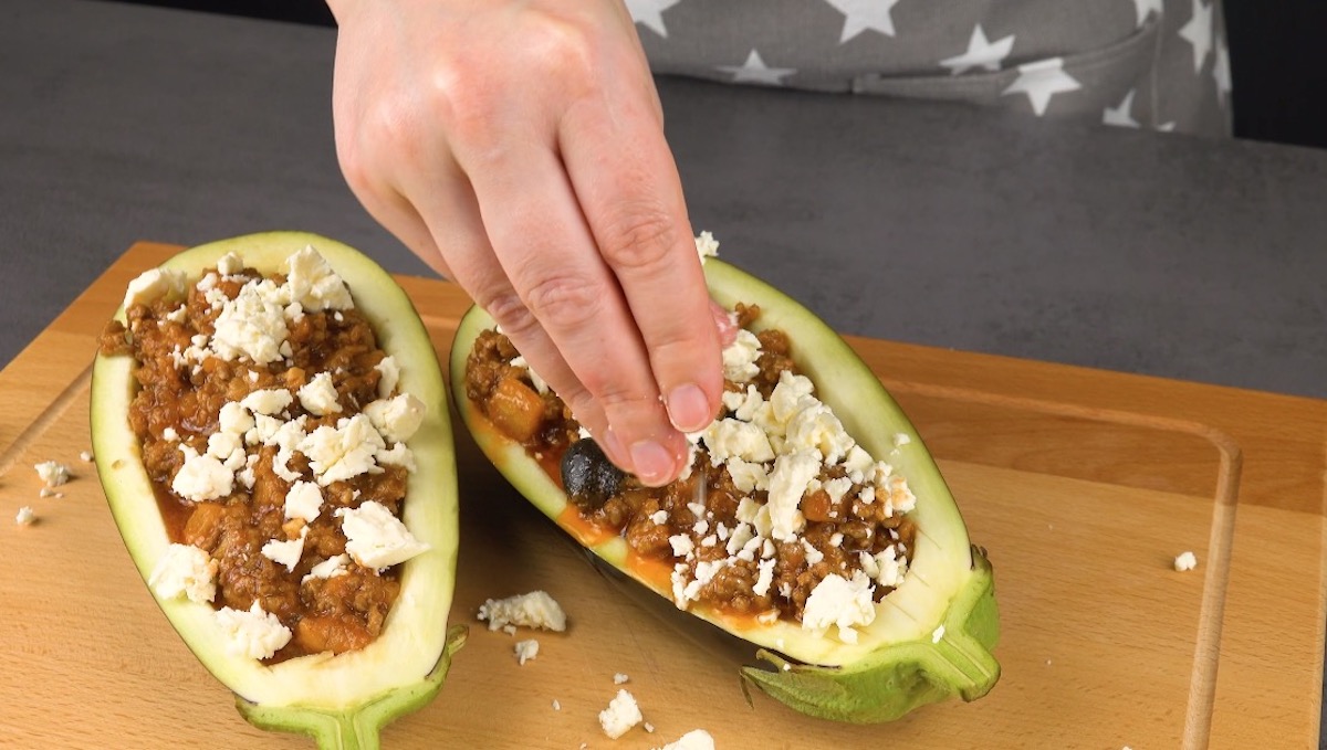 Feta-Käse wird über 2 mit einer Hackfleisch-Mischung gefüllten Auberginenhälften verteilt.
