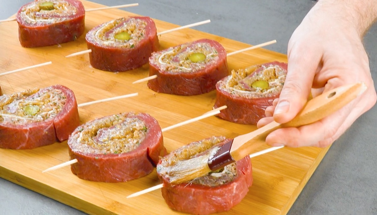 Rouladenspieße auf Holzbrett werden mit Marinade bestrichen