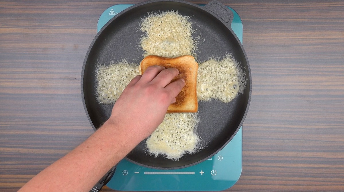 Auf ein Kreuz aus Parmesan in einer Pfanne wird das Toastbrot in die Mitte gelegt