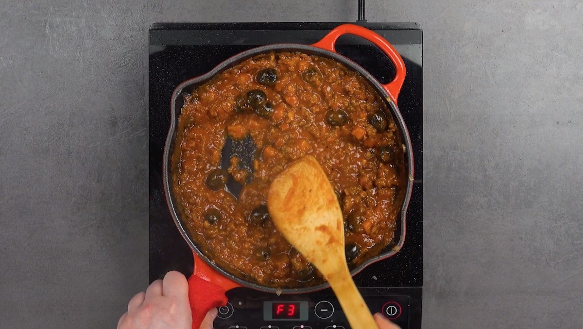 Auberginenwürfel werden mit Oliven, passierten tomaten und Hackfleisch in Pfanne angebraten.