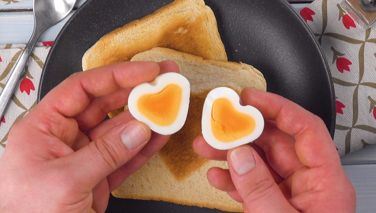 Zwei Herz-Ei-HÃ¤lften werden von HÃ¤nden Ã¼ber zwei Toastscheiben gehalten 