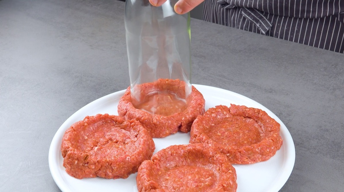 In 4 Burgerpattys aus Hackfleisch wird mit Glasflasche eine Mulde hineingedrÃ¼ckt