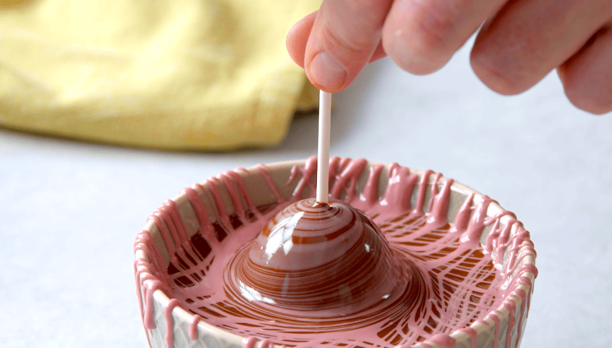 Ein Cake Pop wird in geschmolzene Schokolade getunkt.