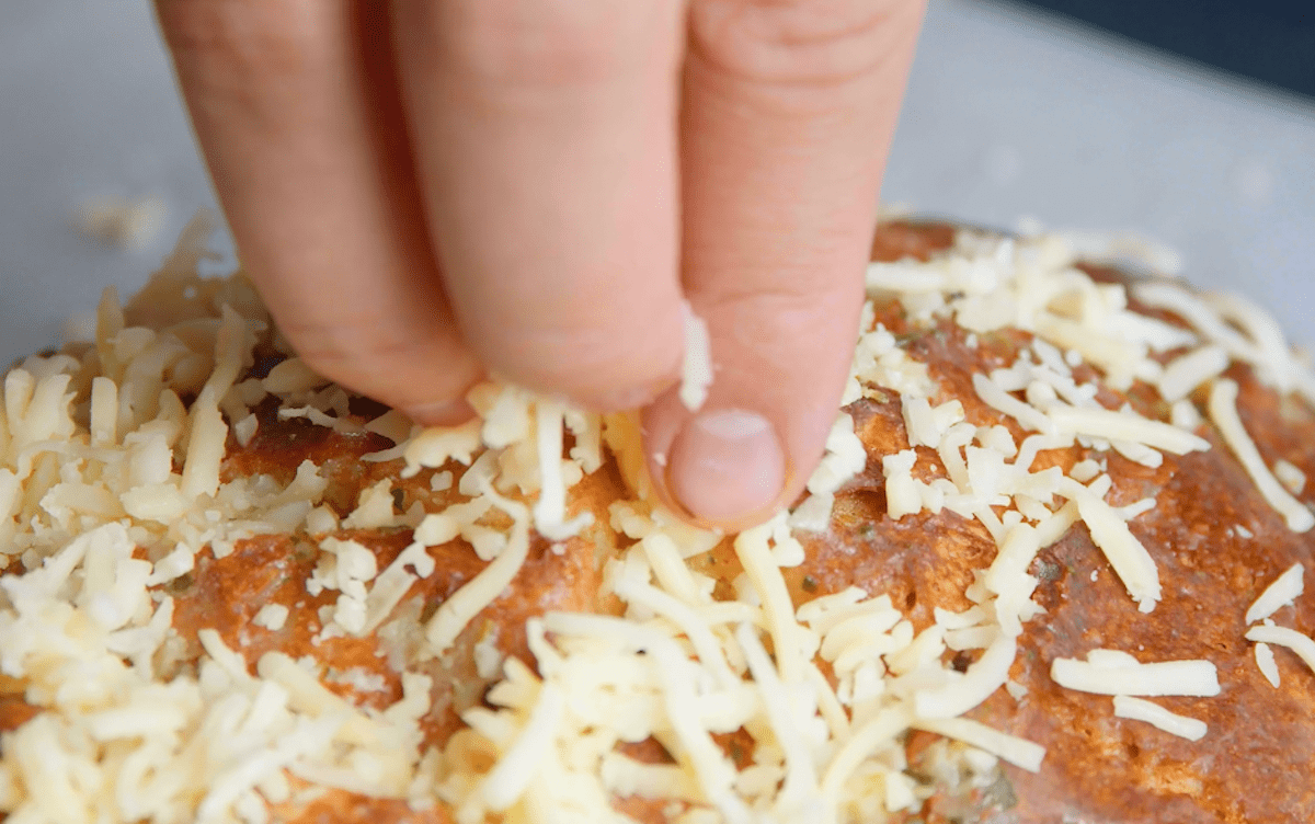 geriebener Mozzarella wird auf Brot verteilt