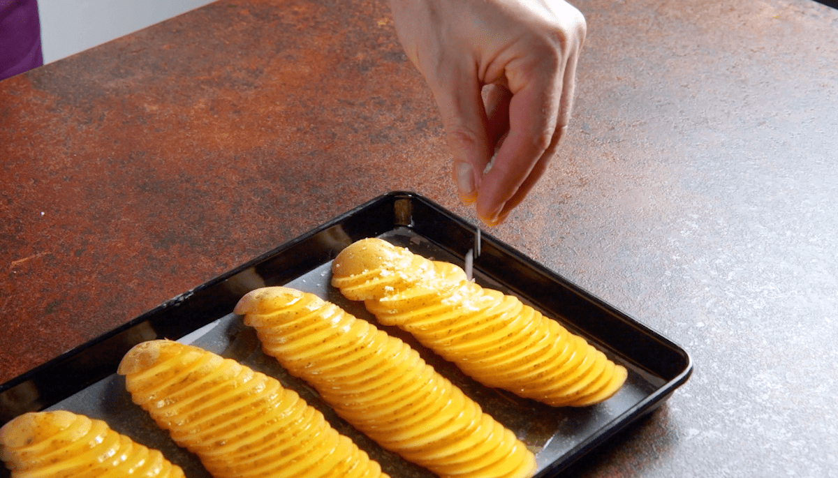Auf einem Backblech gefächerte Kartoffelscheiben werden mit Salz bestreut