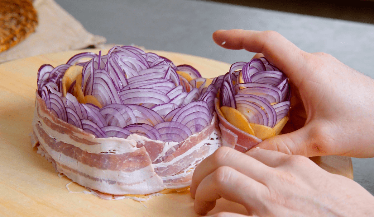 Zwiebelscheiben, Bacon und Kartoffelscheiben werden zu einer großen Rolle zusammengerollt