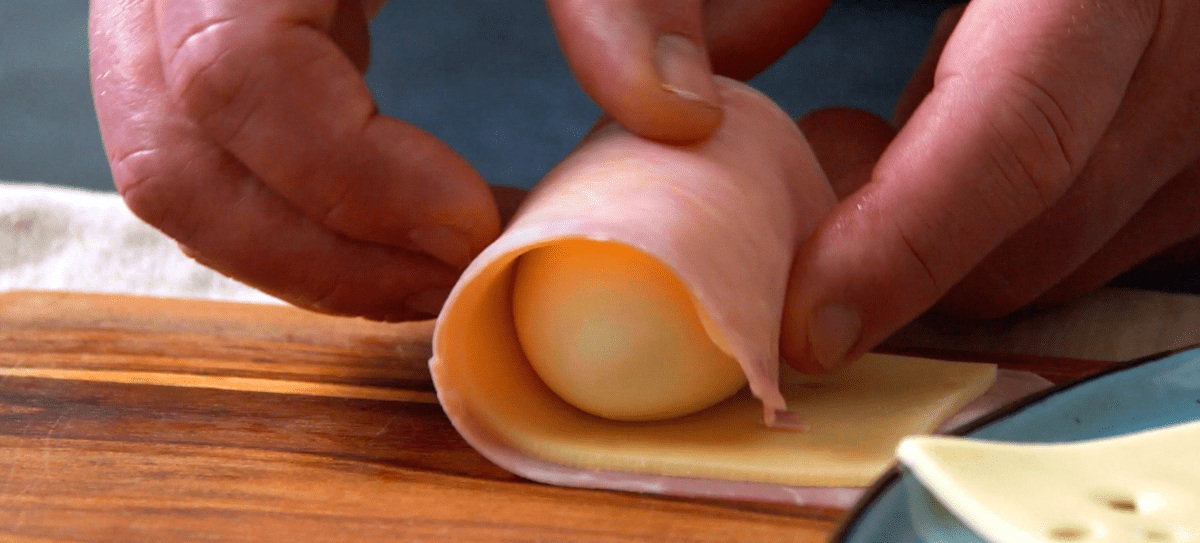 Ei wird in Schinken und Käse eingerollt.