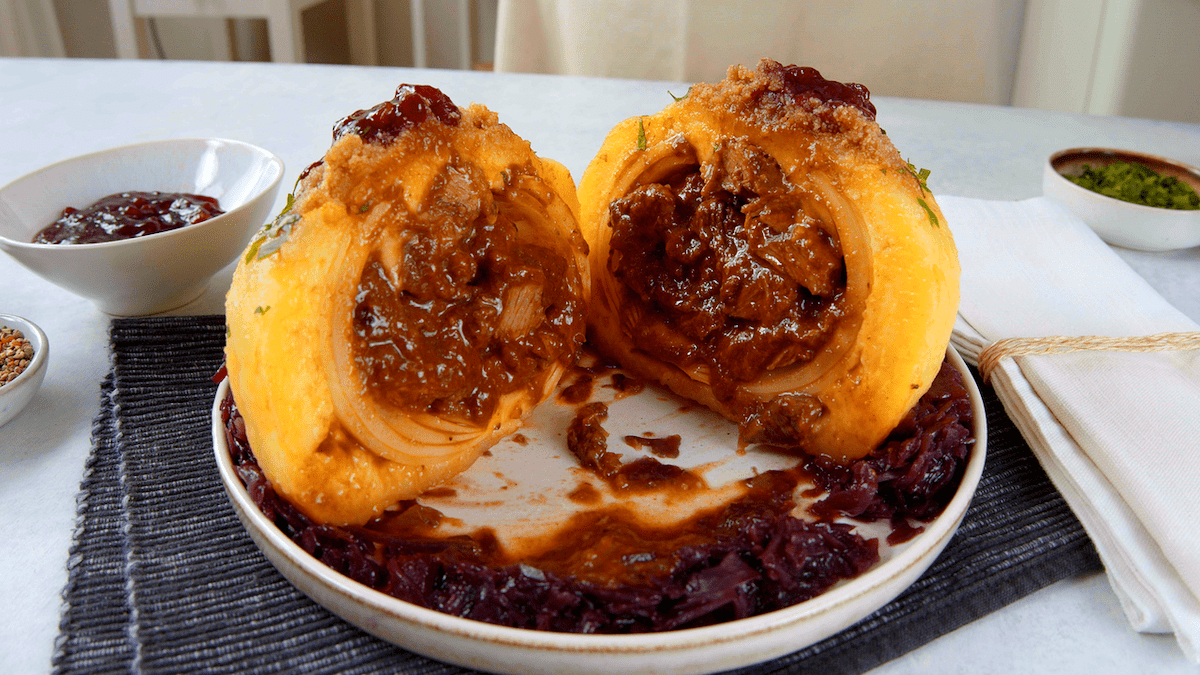 Eine mit Rinderragout gefüllte Zwiebel in Kloßteig auf Rotkohl mit Semmelbutter