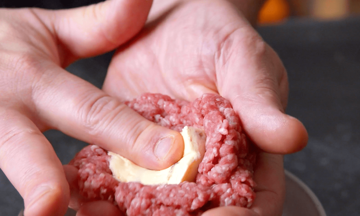 Hackfleisch und Weichkäse werden auf einer Hand verteilt