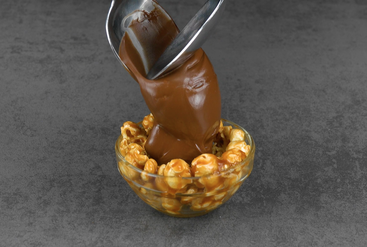Halber Popcorn-Ball wird mithilfe eines Löffels mit Schokocreme gefüllt