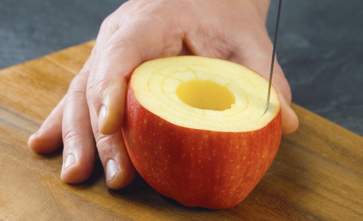 AusgehÃ¶hlter Apfel, von dem der Deckel angeschnitten wurde, wird mit Messer rundherum eingeschnitten