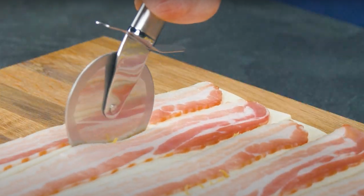 Baconstreifen werden auf BlÃ¤tterteig gelegt und mit Pizzaschneider an RÃ¤ndern der Speckstreifen entlang geschnitten