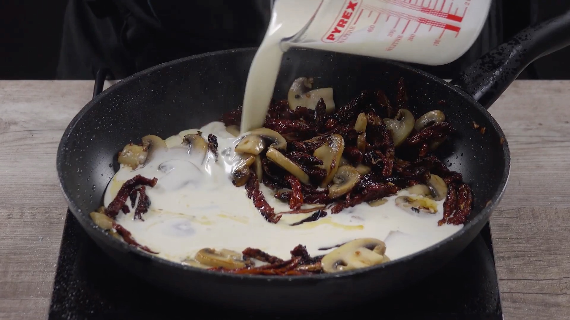 Milch wird zu getrockneten Tomaten und Champignons in eine Pfanne gegossen
