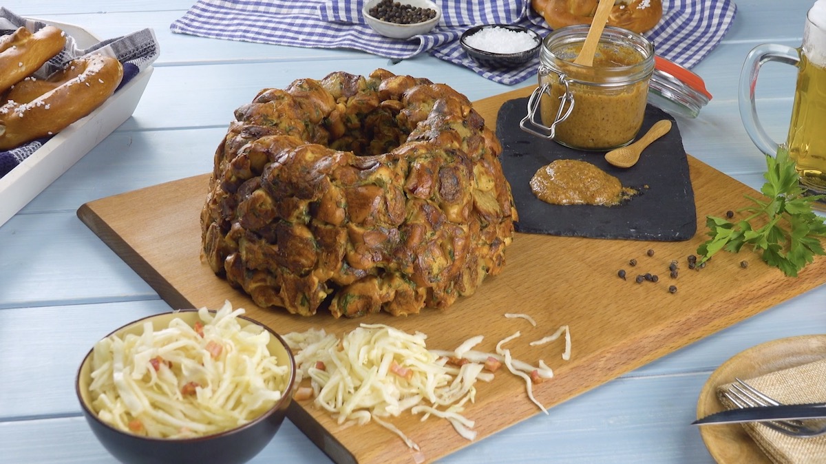 Herzhafte Gugelhupf aus Brezeln und Bratwürsten auf Holzbrett mit süßem Senf und Krautsalat