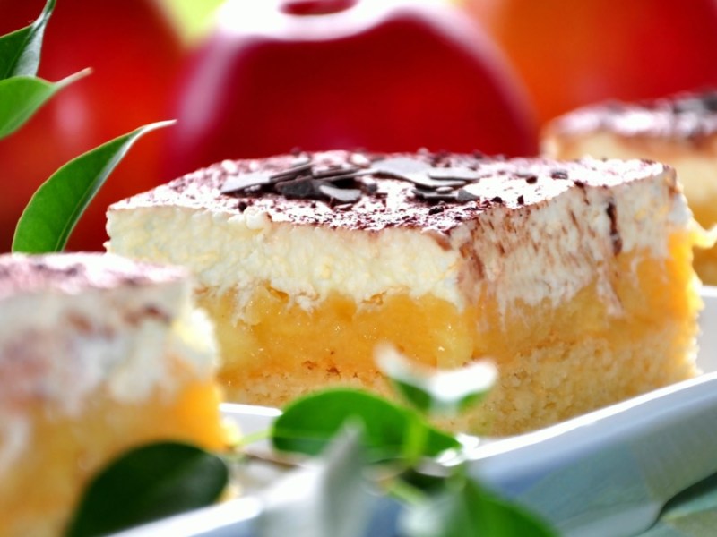 3 Stücken Apfelmus-Schmand-Kuchen auf einer Servierplatte, im Hintergrund rote Äpfel.