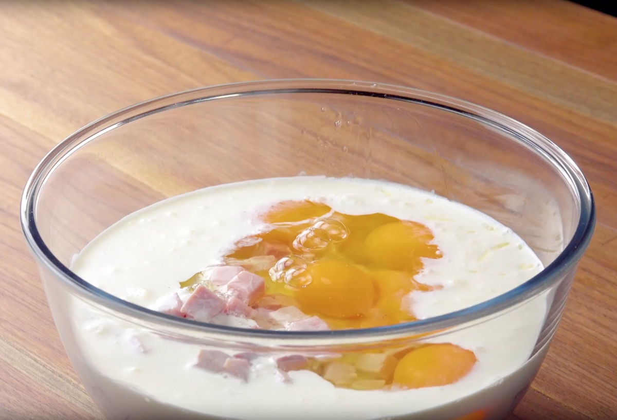 Geriebener Mozzarella, Eier, Sahne und gewÃ¼rfelter Kochschinken werden in SchÃ¼ssel miteinander vermengt.