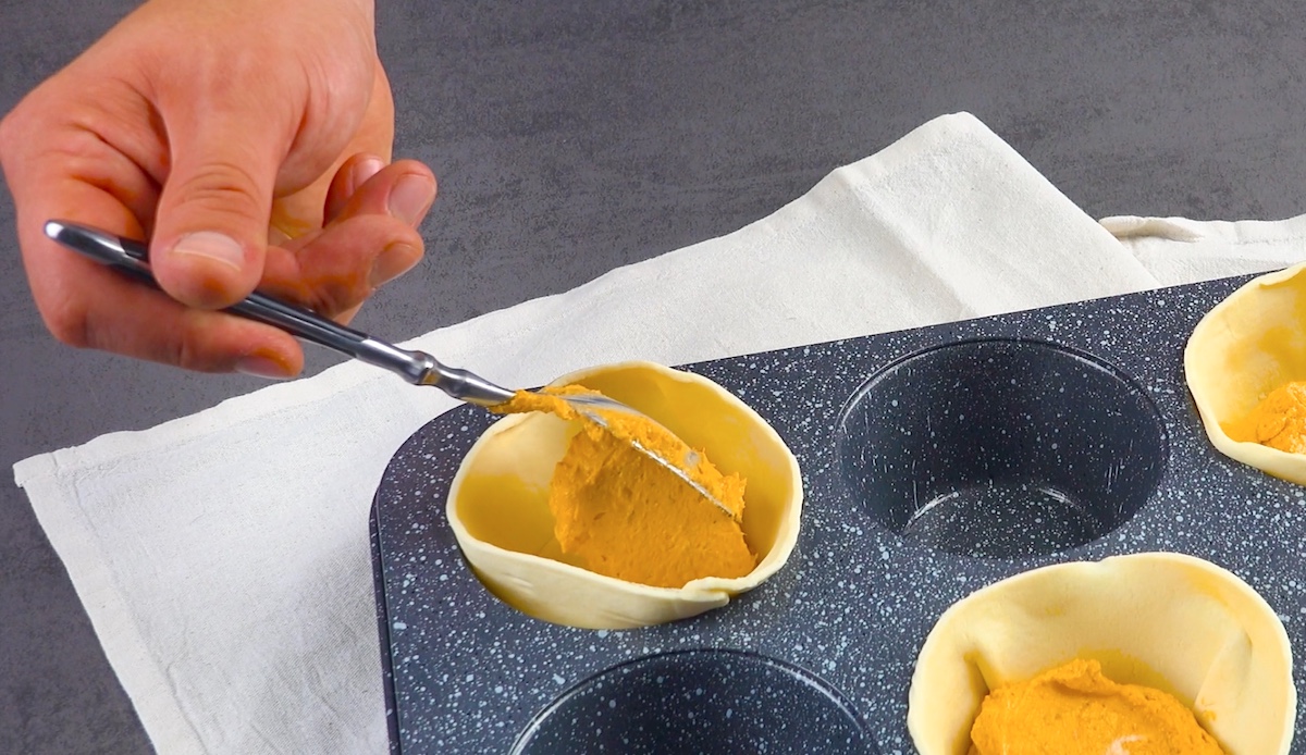 Füllung aus Frischkäse und Pesto wird in Blätterteig in Muffinformen gegeben