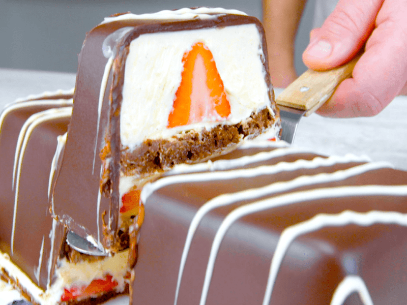 Schoko-Dessert mit Vanillecreme und Erdbeeren, aus dem ein Stück geschnitten wird.