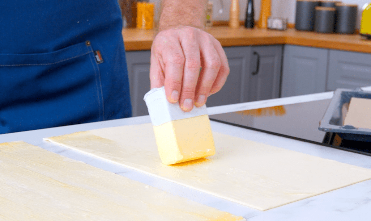 Butter wird auf ausgerollten Blätterteig verstrichen