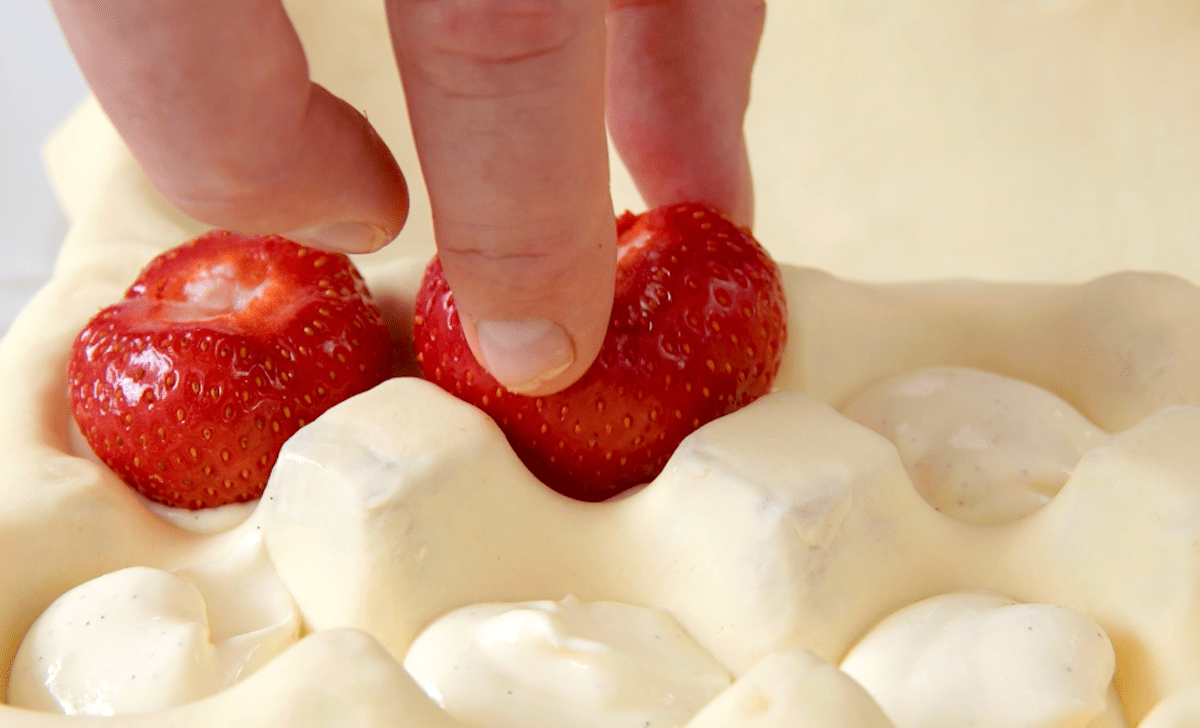 Eine Erdbeere wird in FrischkÃ¤secreme gedrÃ¼ckt