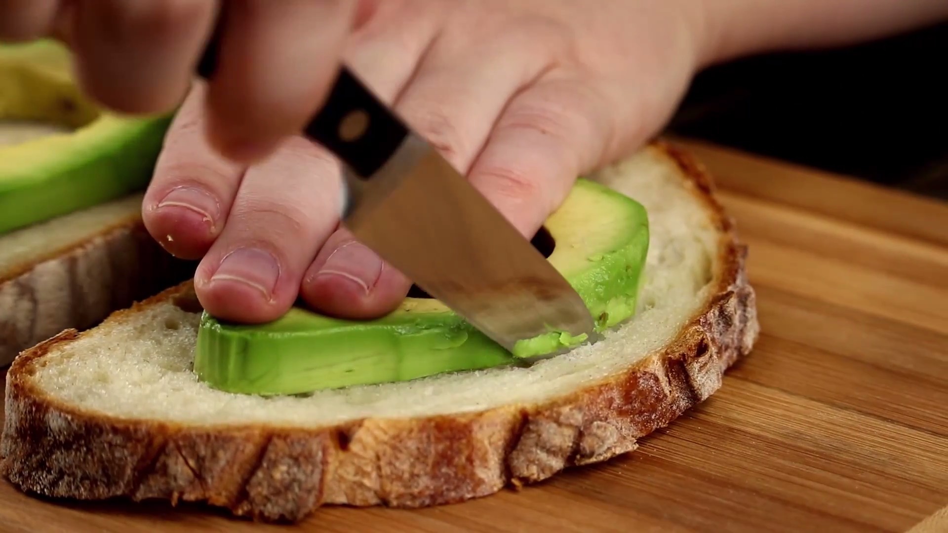 Avocadoscheibe wird auf Brotscheibe gelegt und mit Messer ausgeschnitten