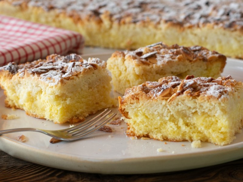 3 Stücke Butterkuchen ohne Hefe auf einem Teller, im Hintergrund das Belch mit dem Kuchen und ein Geschirrtuch.