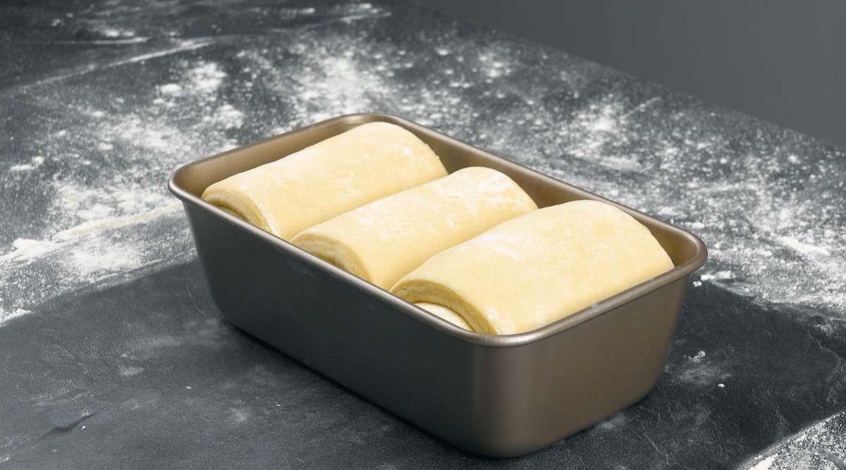 Teigrollen fÃ¼r das Croissant-Brot werden in Backform gelegt.