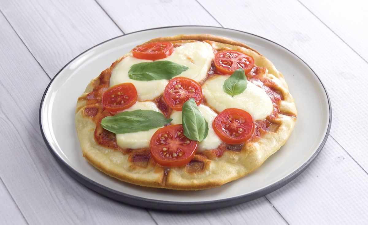 Eine Pizza aus dem Waffeleisen mit Mozzarella, Tomaten und Basilikum auf einem Teller. 