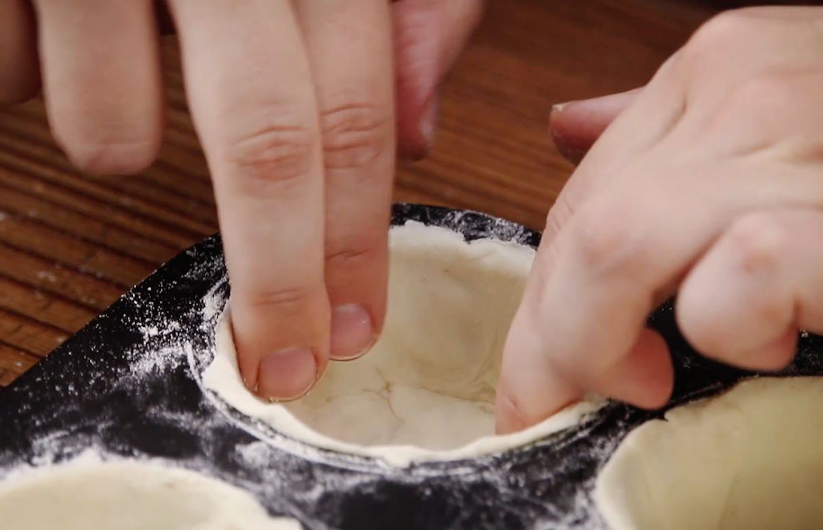 Blätterteig wird in Mulden von Muffinblech gedrückt