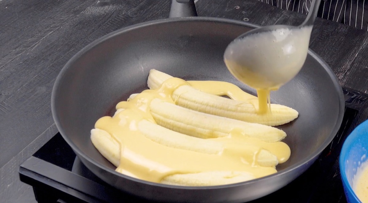 Halbierte Bananen in Pfanne werden mit Pfannkuchenteig Ã¼bergossen