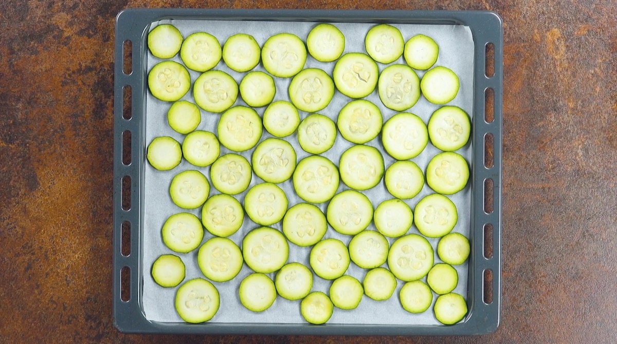 Zucchinischeiben werden gleichmäßig auf einem mit Backpapier belegtem Backblech verteilt