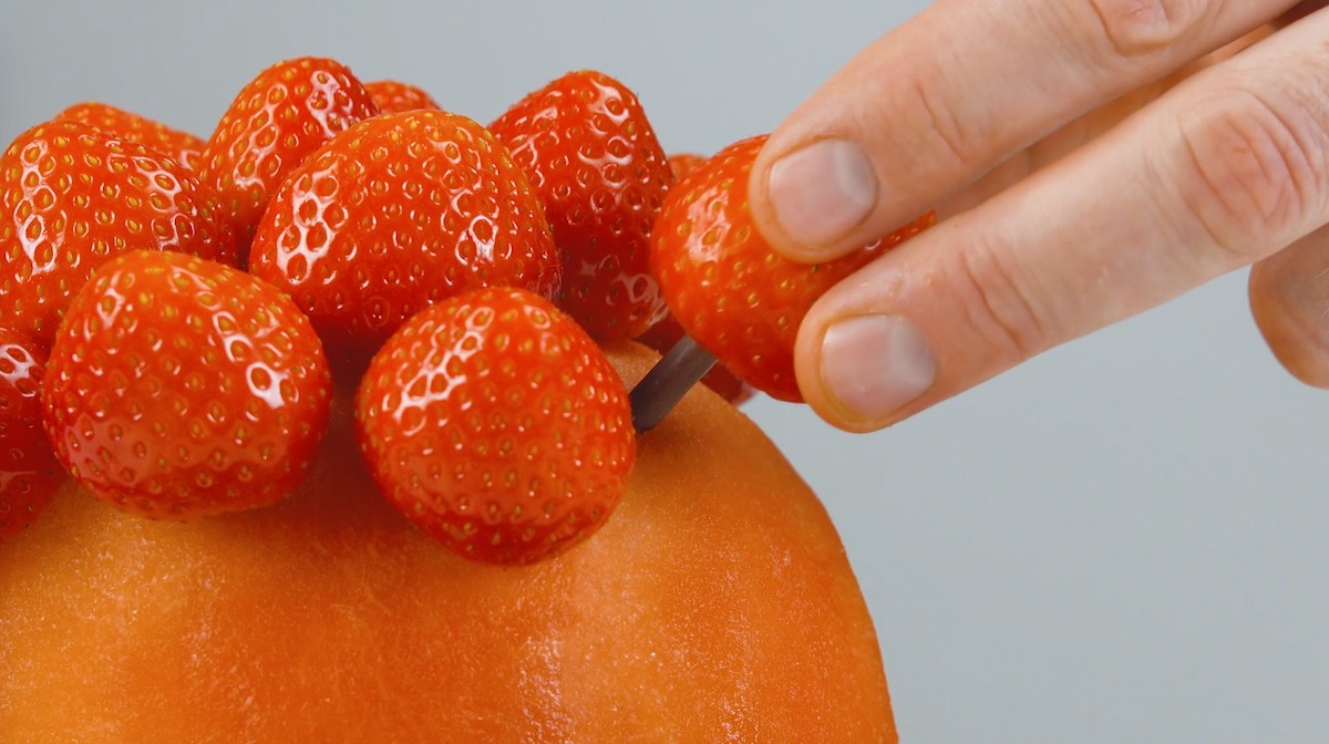 Erdbeeren werden mit Hilfe von Mikado-StÃ¤bchen in die Melone gesteckt