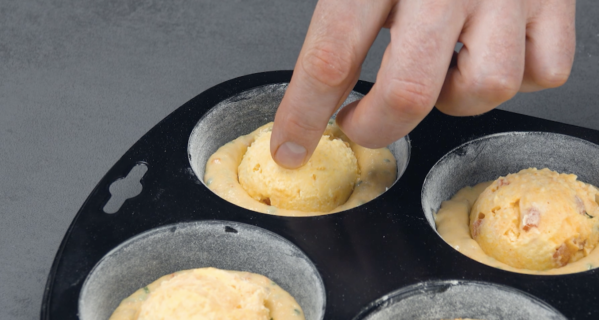 Je eine gefrorene Käsekugel wird in Teig in Muffinform gedrückt