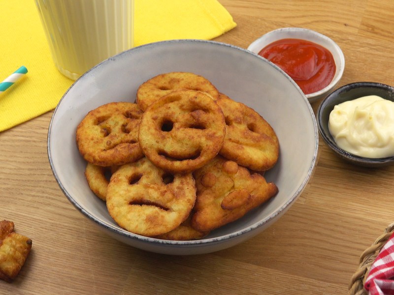 Emoji-Pommes in einer Schüssel, daneben Schüsseln mit Ketchup und Mayo.