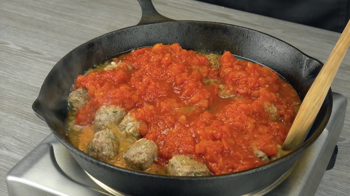 HackbÃ¤llchen werden mit gehackten Tomaten in Pfanne angebraten