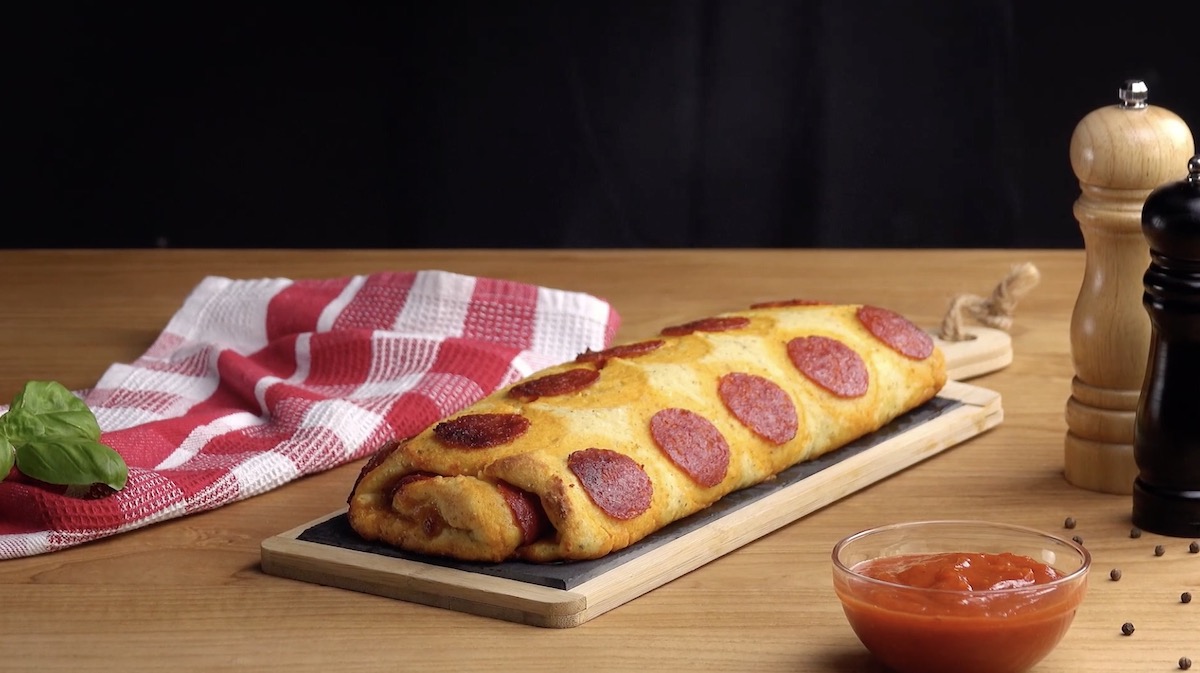 Eine Pizza aus Kartoffelbrei auf einem Brett. Daneben Salz- und Pfeffermühlen und eine Schale mit Ketchup.