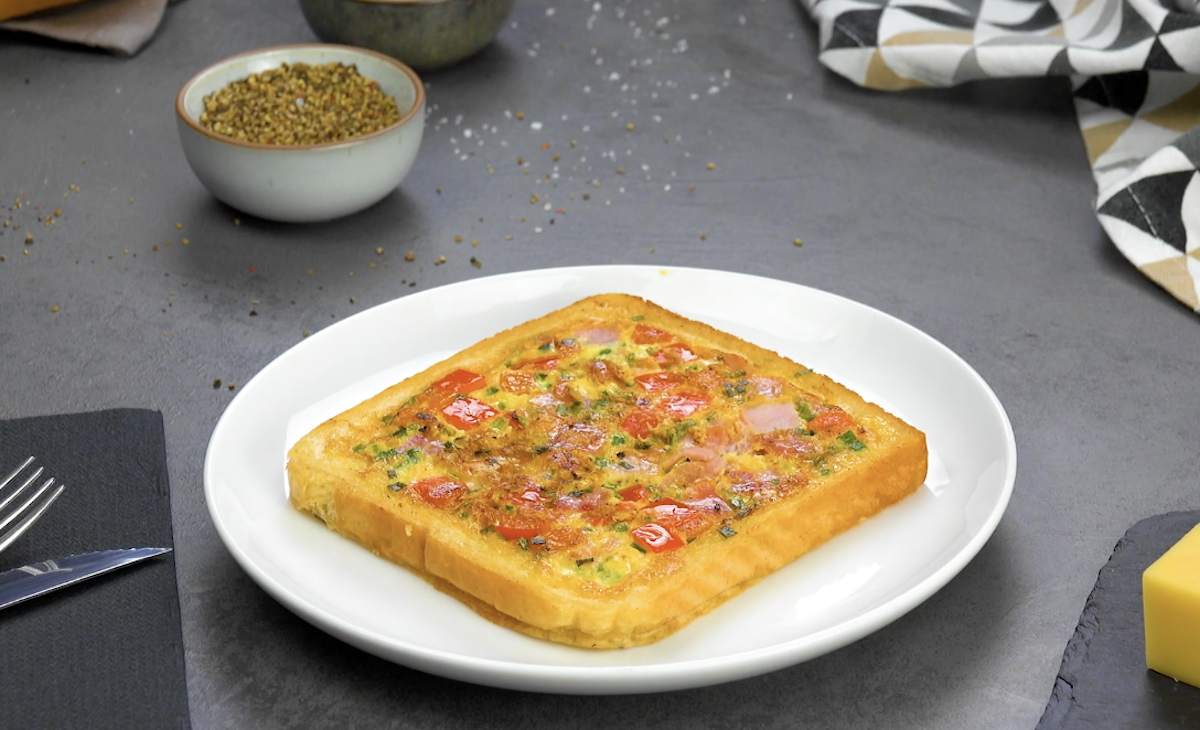 Ein Pizza-Toast auf einem Teller, drumherum Zutaten und Küchenutensilien.
