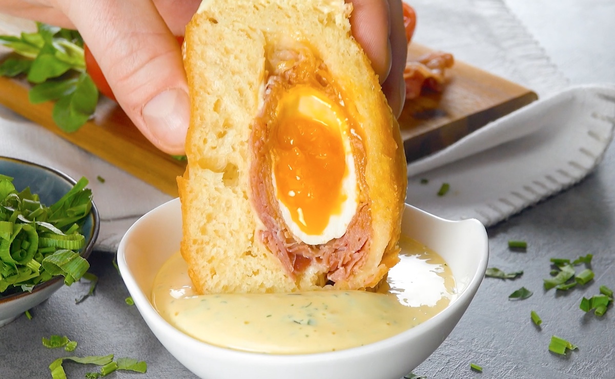 Pochiertes Ei mit Schinken in Donut-Teig, das in Sauce hollandaise getaucht wird